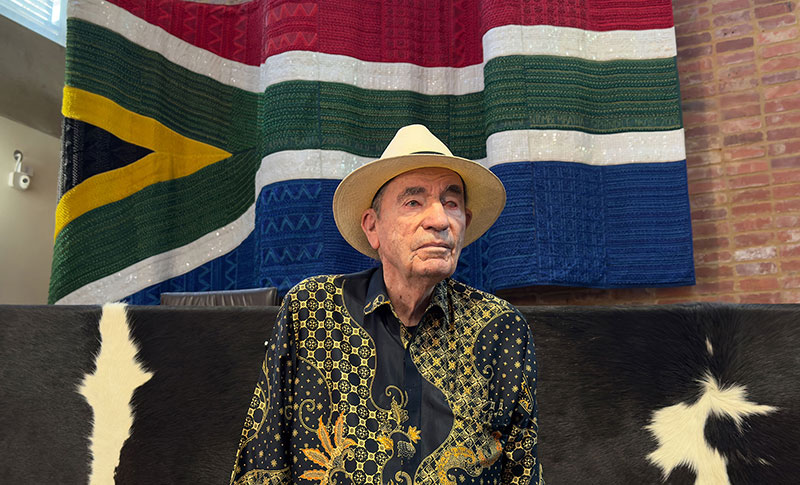 Albie in ConCourt main court chamber with beaded flag and cow hides in background.